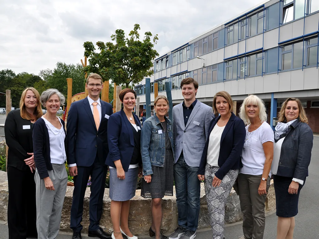 Neun Erwachsene stehen für ein Gruppenfoto vor dem Schulgebäude.